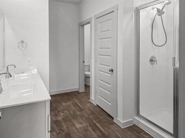 bathroom featuring a stall shower, toilet, wood finished floors, a sink, and baseboards