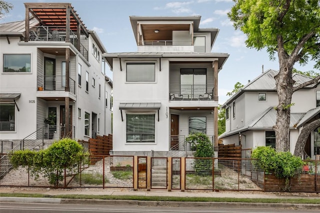 1103 12th St E, Austin, TX 78702 - modern home with a balcony, a fenced front yard, a standing seam roof, stucco siding, and metal roof