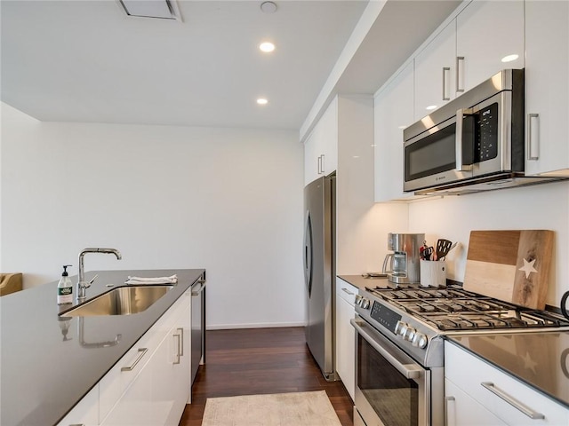 kitchen with stainless steel appliances, a sink, dark countertops, dark wood-style flooring, and white cabinetry