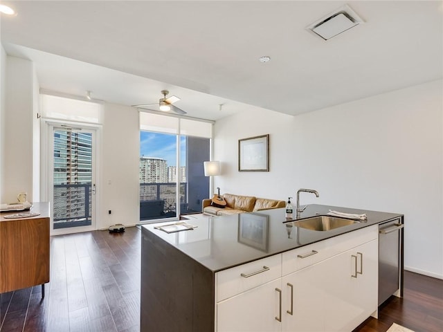 kitchen with a sink, dark wood-style floors, an island with sink, stainless steel dishwasher, and floor to ceiling windows