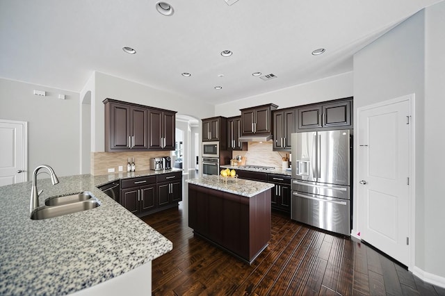 4121 Vinalopo Dr, Austin, TX 78738 - kitchen featuring appliances with stainless steel finishes, arched walkways, dark brown cabinets, under cabinet range hood, and a kitchen island