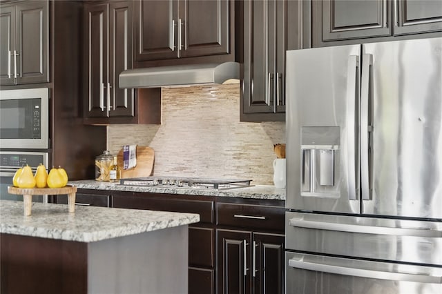 4121 Vinalopo Dr, Austin, TX 78738 - kitchen featuring stainless steel appliances, wall chimney range hood, dark brown cabinetry, decorative backsplash, and light stone countertops