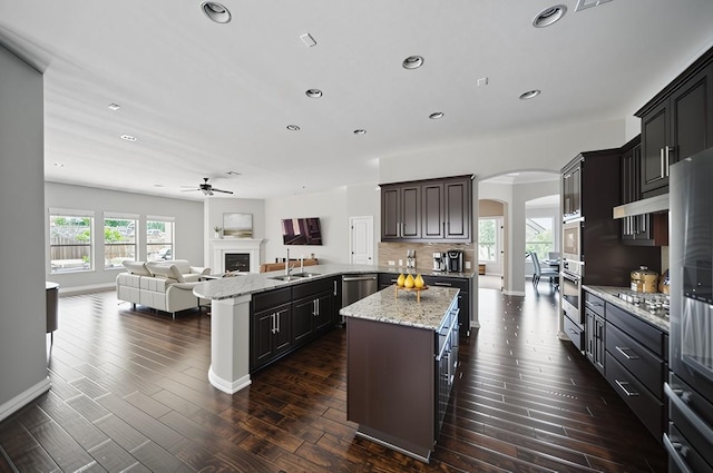 4121 Vinalopo Dr, Austin, TX 78738 - kitchen featuring arched walkways, open floor plan, a fireplace, a kitchen island, and stainless steel appliances