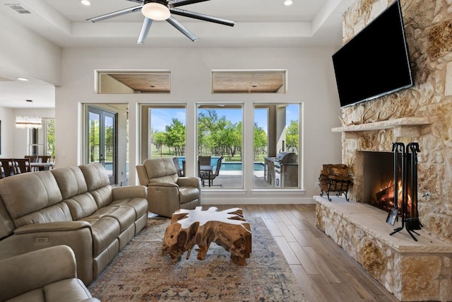 10900 Ranch Road 1323, Johnson City, TX 78636 - living area featuring hardwood / wood-style floors, a ceiling fan, a stone fireplace, a tray ceiling, and recessed lighting