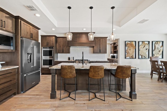 10900 Ranch Road 1323, Johnson City, TX 78636 - kitchen with appliances with stainless steel finishes, a tray ceiling, decorative backsplash, light wood finished floors, and a kitchen bar