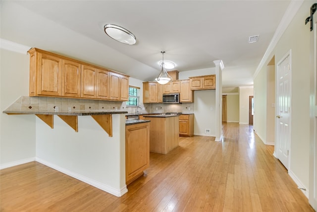104 Springfield, Horseshoe Bay, TX 78657 - kitchen featuring stainless steel microwave, a peninsula, light wood-type flooring, backsplash, and crown molding