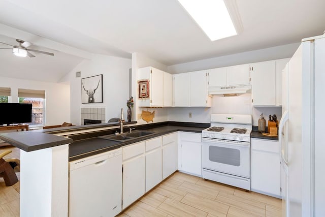 kitchen featuring white appliances, under cabinet range hood, dark countertops, a sink, and a peninsula