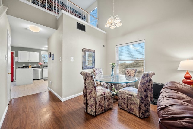 dining room featuring baseboards, wood finished floors, a chandelier, plenty of natural light, and a towering ceiling