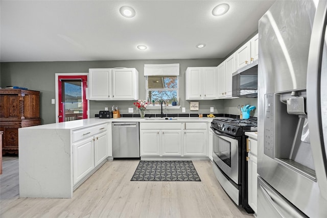 kitchen featuring stainless steel appliances, a sink, a peninsula, light wood-style floors, and white cabinetry