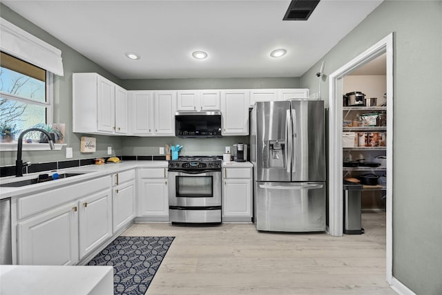 kitchen featuring stainless steel appliances, a sink, white cabinetry, light countertops, and light wood finished floors