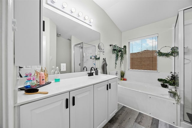 full bathroom featuring vaulted ceiling, a shower stall, vanity, a garden tub, and wood finished floors