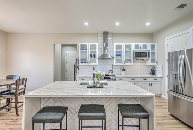 171 Eely Rd, Mcdade, TX 78650 - kitchen with stainless steel appliances, wall chimney range hood, a kitchen bar, light wood-type flooring, and white cabinetry