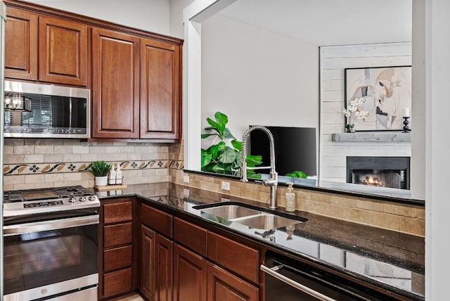 2930 Grand Oaks Loop Unit 401, Cedar Park, TX 78613 - kitchen featuring stainless steel appliances, a sink, backsplash, a large fireplace, and dark stone countertops