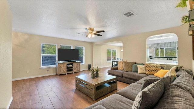 living area featuring arched walkways, a ceiling fan, baseboards, wood finished floors, and a textured ceiling