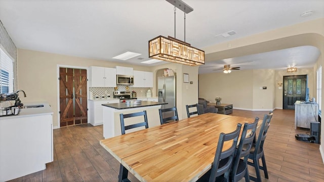 dining room with dark wood finished floors, ceiling fan, baseboards, and arched walkways