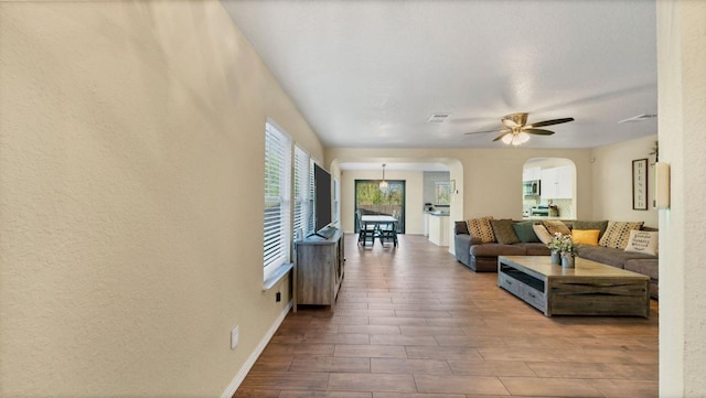living area with ceiling fan, arched walkways, wood finished floors, and baseboards