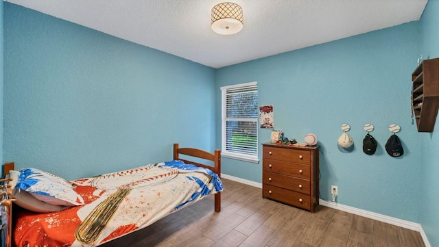 bedroom with a textured wall, wood finished floors, baseboards, a textured ceiling, and ceiling fan