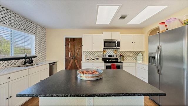kitchen featuring stainless steel appliances, a sink, a center island, white cabinets, and decorative backsplash