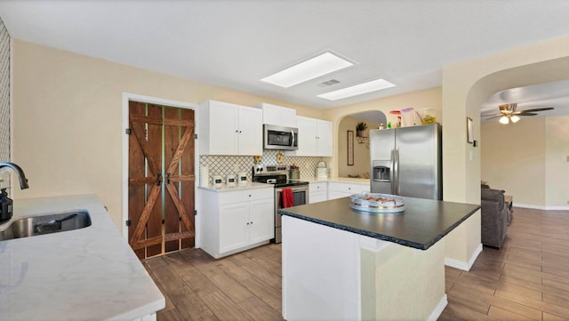 kitchen featuring appliances with stainless steel finishes, arched walkways, a sink, and wood finished floors