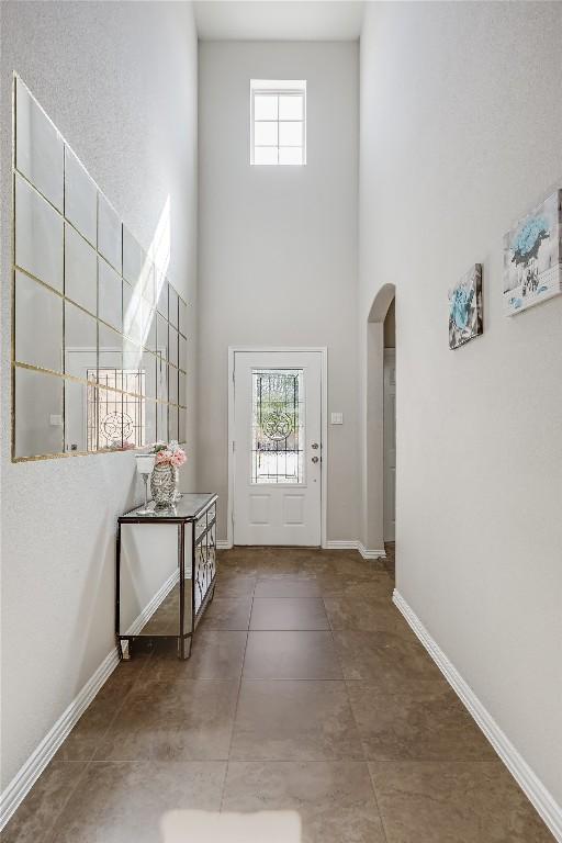 doorway to outside with a towering ceiling, arched walkways, healthy amount of natural light, and baseboards