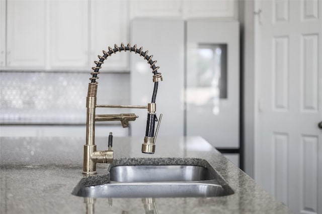 kitchen view of a sink, white cabinetry, and stone countertops