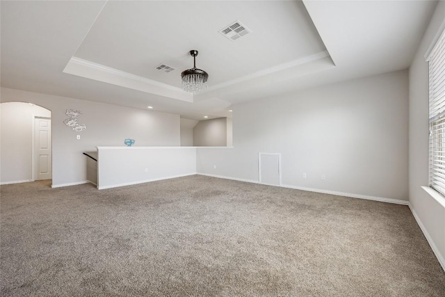 carpeted spare room featuring a raised ceiling, arched walkways, and baseboards