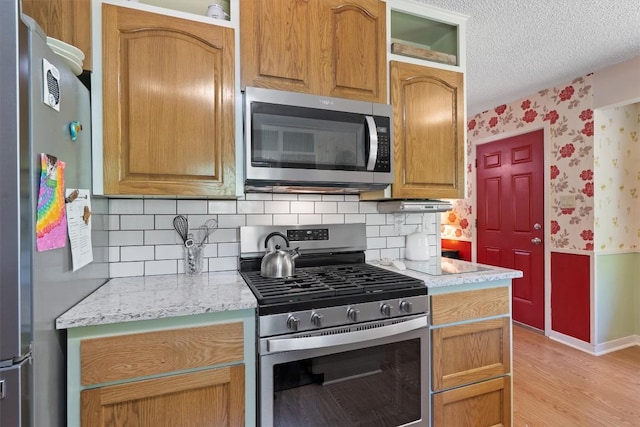 kitchen featuring stainless steel appliances, wallpapered walls, light wood-style flooring, baseboards, and a textured ceiling