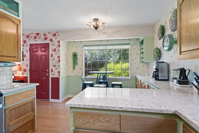 kitchen with wallpapered walls, a textured ceiling, light wood-style floors, a wainscoted wall, and a peninsula