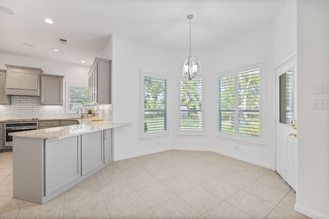kitchen featuring oven, gray cabinets, stovetop, decorative backsplash, and light stone countertops