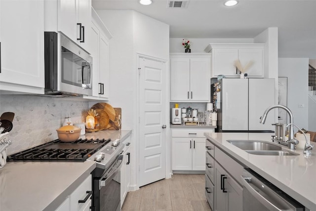 kitchen featuring appliances with stainless steel finishes, a sink, light countertops, white cabinetry, and recessed lighting