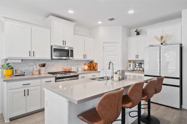 kitchen featuring freestanding refrigerator, stainless steel microwave, range, a sink, and an island with sink