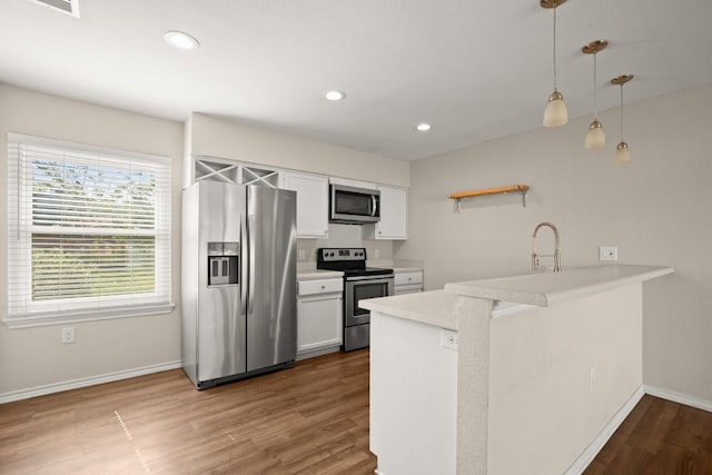 kitchen with appliances with stainless steel finishes, a peninsula, wood finished floors, baseboards, and light countertops