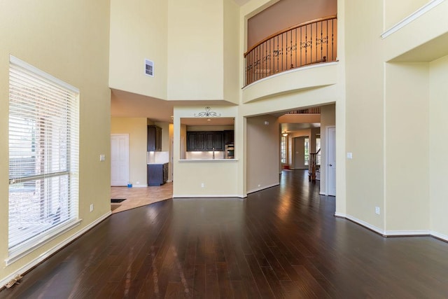 unfurnished living room with hardwood / wood-style flooring, baseboards, and a towering ceiling
