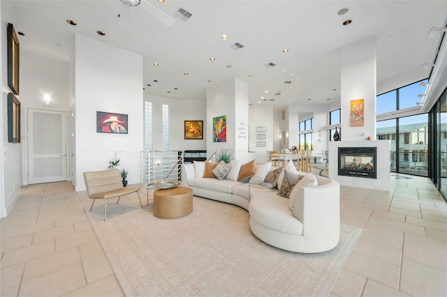 living area with light tile patterned floors, a multi sided fireplace, recessed lighting, and a towering ceiling