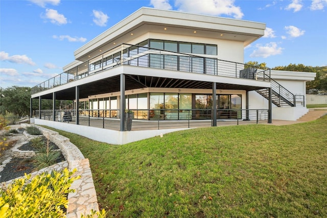 rear view of property featuring stairway, stucco siding, and a lawn