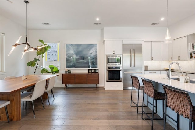 2500 Cedarview Dr, Austin, TX 78704 - kitchen with built in appliances, dark wood-style floors, a breakfast bar area, white cabinetry, and pendant lighting