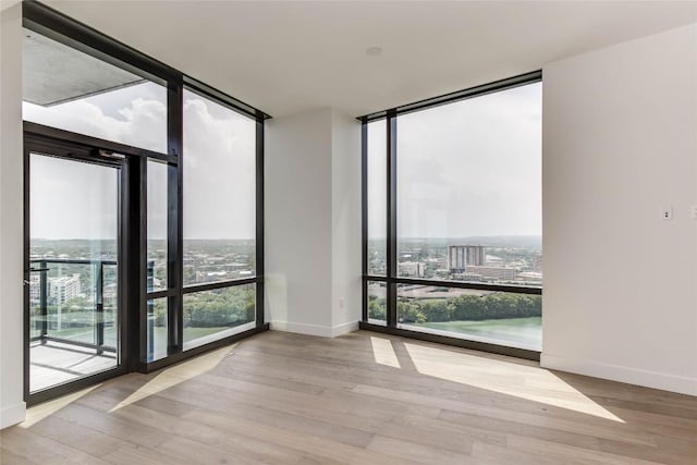 unfurnished room with a wall of windows, plenty of natural light, wood finished floors, and baseboards