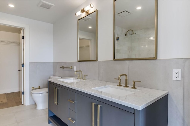 full bath featuring a tile shower, toilet, tile walls, double vanity, and recessed lighting