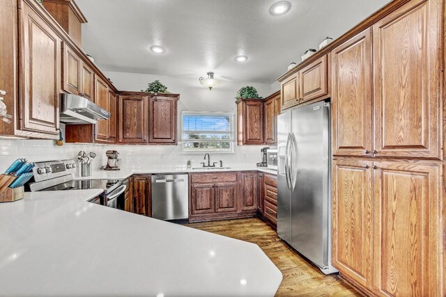 603 Watterson Rd Unit B, Bastrop, TX 78602 - kitchen with appliances with stainless steel finishes, under cabinet range hood, light wood-style flooring, a sink, and tasteful backsplash