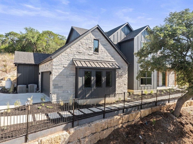view of front of property with an attached garage, fence, stone siding, board and batten siding, and central AC
