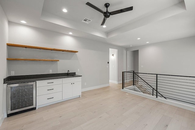 indoor wet bar featuring wine cooler, ceiling fan, a tray ceiling, light wood finished floors, and recessed lighting