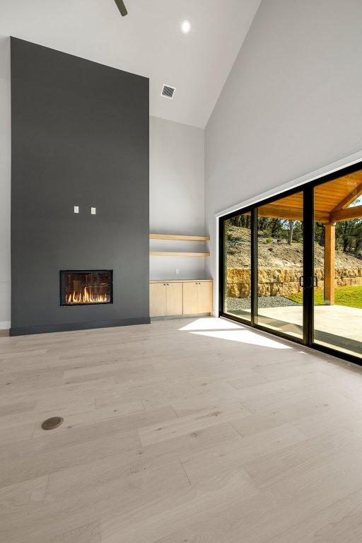 spare room with high vaulted ceiling, a large fireplace, and wood finished floors