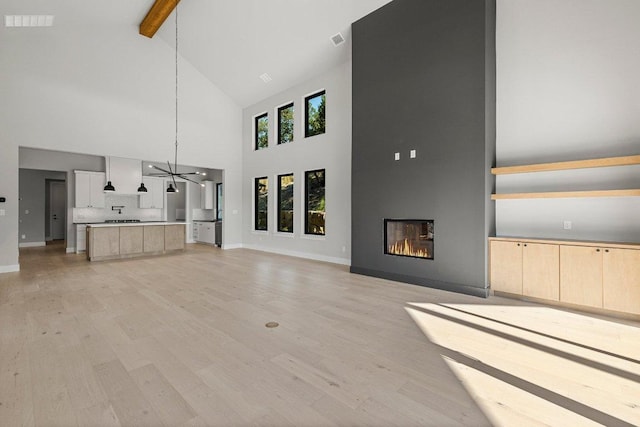 unfurnished living room featuring high vaulted ceiling, beamed ceiling, light wood finished floors, a fireplace, and baseboards