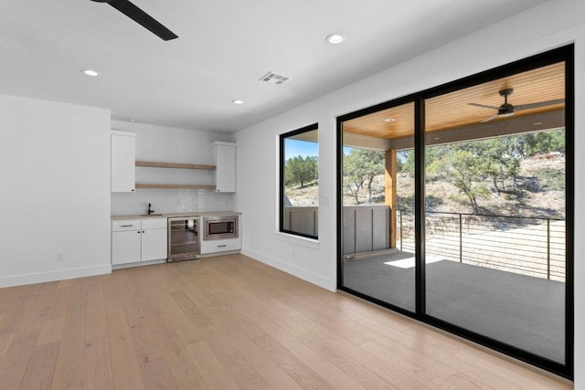 19634 Thurman Bend Rd, Spicewood, TX 78669 - kitchen featuring wine cooler, ceiling fan, stainless steel microwave, white cabinets, and open shelves