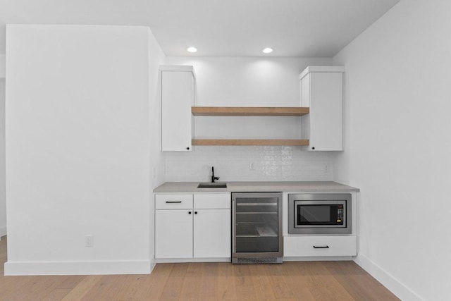 19634 Thurman Bend Rd, Spicewood, TX 78669 - bar area featuring beverage cooler, stainless steel microwave, decorative backsplash, light wood-style flooring, and recessed lighting
