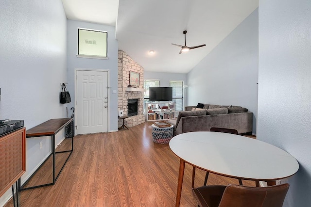 living room featuring wood finished floors, ceiling fan, high vaulted ceiling, and a stone fireplace
