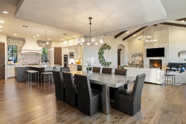 308 Duckhorn Pass, Austin, TX 78738 - dining space with a chandelier, a stone fireplace, dark wood-style floors, arched walkways, and recessed lighting