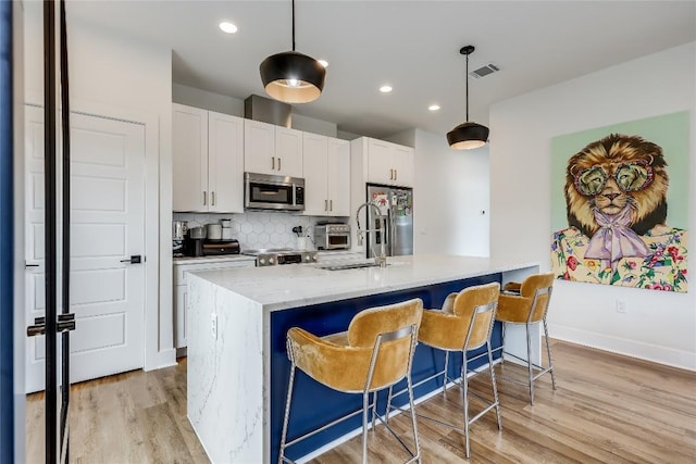 8603 Big Horn Cir, Lago Vista, TX 78645 - kitchen with appliances with stainless steel finishes, light wood finished floors, decorative backsplash, a kitchen island with sink, and white cabinetry