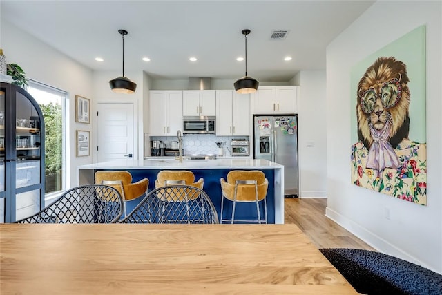 8603 Big Horn Cir, Lago Vista, TX 78645 - kitchen featuring stainless steel appliances, tasteful backsplash, white cabinets, decorative light fixtures, and light wood-style floors