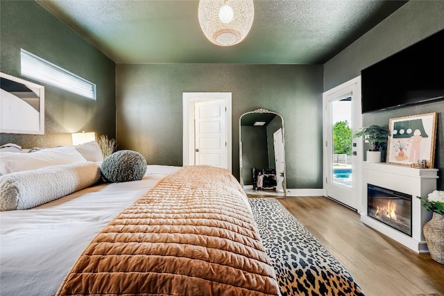 8603 Big Horn Cir, Lago Vista, TX 78645 - bedroom with access to outside, wood finished floors, a glass covered fireplace, a textured wall, and a textured ceiling